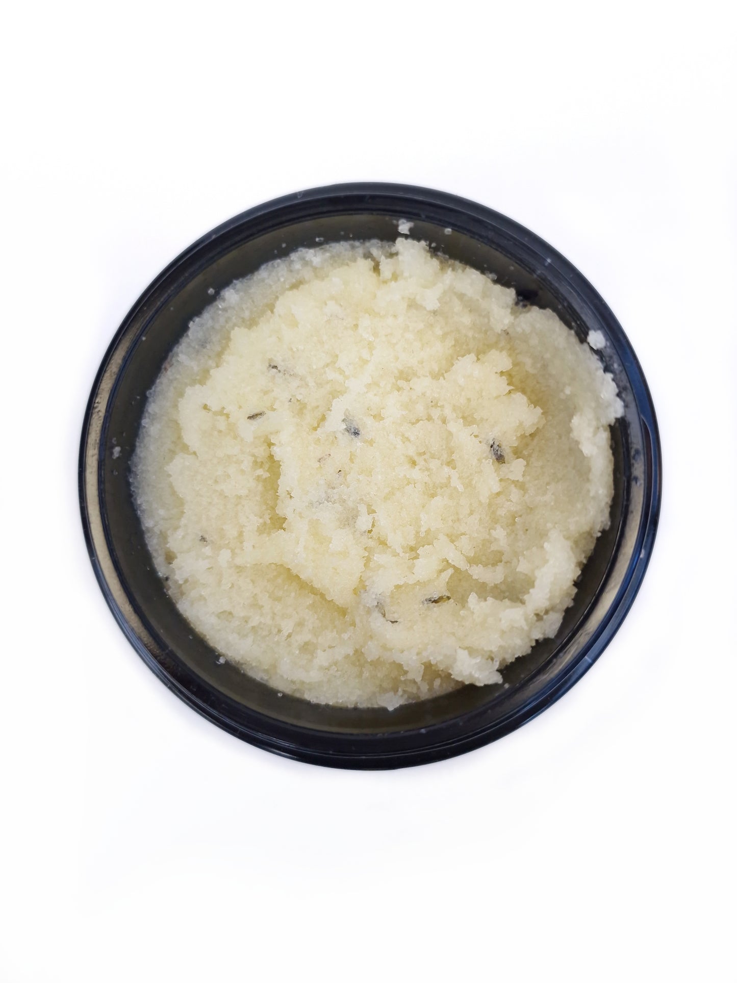 Close-up of light yellow salt body scrub in a jar, showing its texture and natural ingredients on white background.