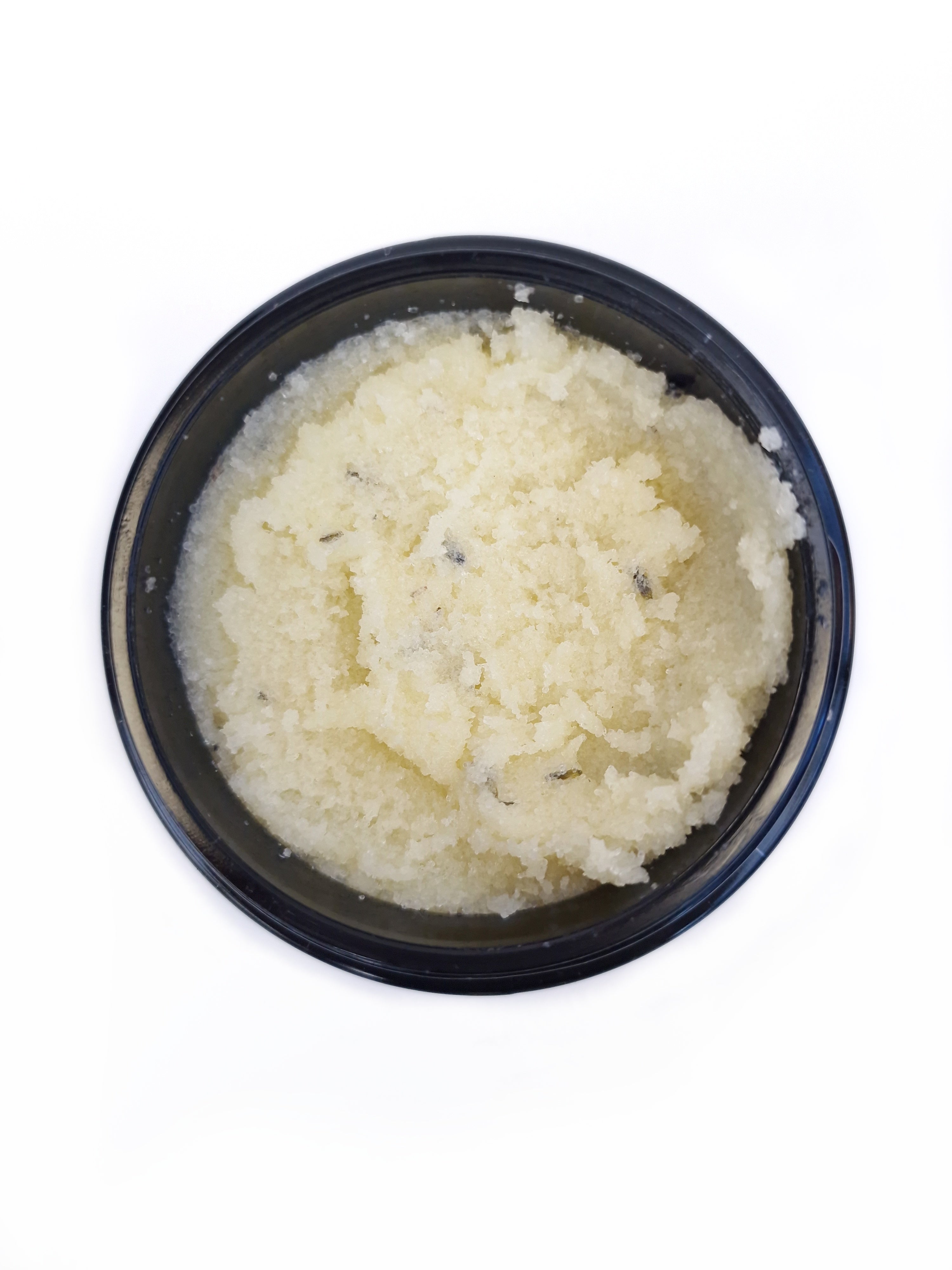Close-up of light yellow salt body scrub in a jar, showing its texture and natural ingredients on white background.